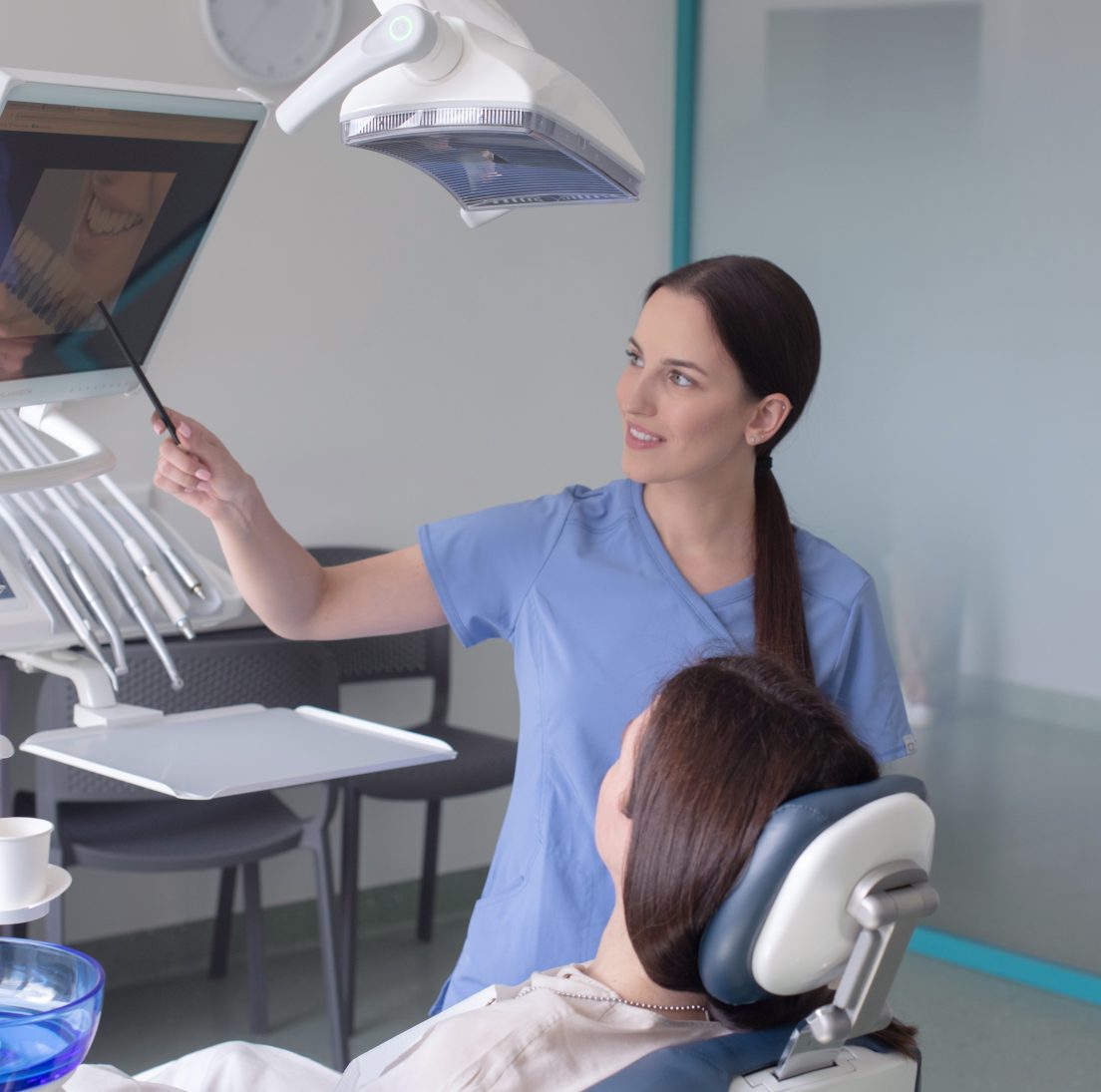 Odontologė Iveta rodo estetinio plombavimo pavyzdį ekrane